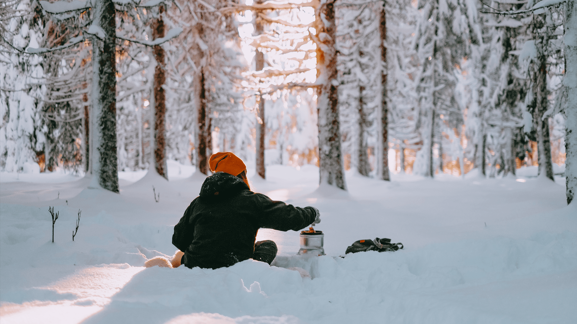 En kvinna sitter i snön och lagar mat på ett trangiakök